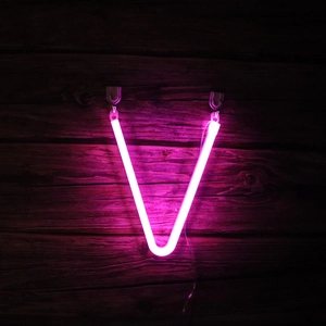 Pink LED neon light letter V glowing on dark wood wall for decorative holiday ambiance