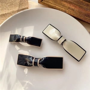 Detailed overhead view of 3pcs bow hair clips in beige and black on white ceramic plate