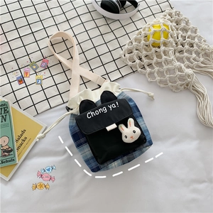 Detail of blue plaid drawstring bucket bag featuring a 3D plush bunny and black front pocket