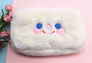Gros plan sur la trousse à maquillage en peluche blanche avec visage souriant brodé
