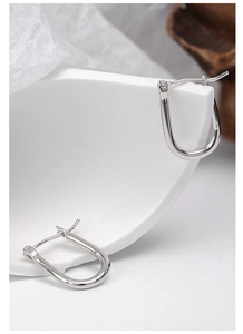 Macro detail of silver U-shaped horseshoe earrings on white geometric minimalist decor