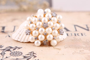Detail view of a pearl and rhinestone flower brooch displayed on a white shell