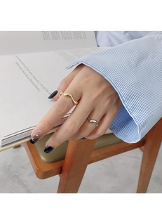 Detail of golden wavy and silver S-shaped rings on hand with striped shirt and book