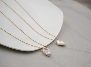 Detail of baroque pearl pendants on gold chains over a ceramic plate