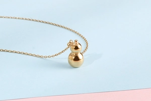 Detailed view of an 18K gold-plated gourd pendant necklace on a bicolored background