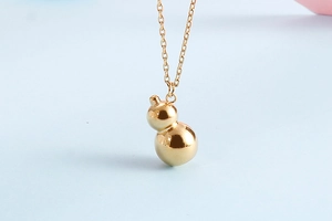 Close-up of polished 18K gold plated gourd pendant necklace on a soft pastel background