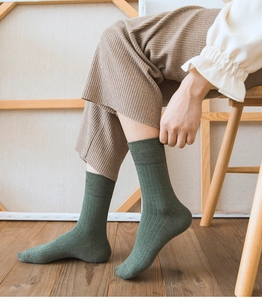 Detail of dark green ribbed knit mid-calf socks worn by a model in a cozy setting