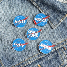 Detail view of NASA inspired enamel pins with SAD and PIZZA text on blue denim fabric