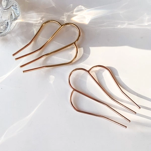 Minimalist metal M-shaped hair pins in gold and rose gold on marble background