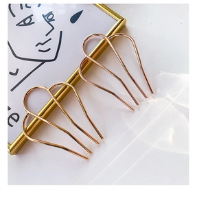 Detailed view of two minimalist M-shaped metal hair forks in gold and rose gold finishes
