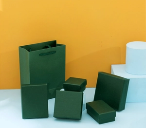 Dark green jewelry gift box set with matching paper bag on a modern white display stand