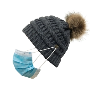 Detail view of dark grey knitted beanie with fluffy pompom and button for mask attachment