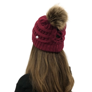 Detail of dark red knit beanie showing cable pattern and brown faux fur pom-pom on top