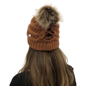 Detail of caramel knit beanie with faux fur pompom and cross-back ponytail opening
