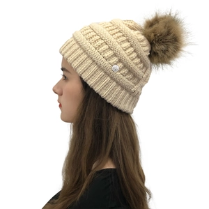Detail of cream knit beanie with brown faux fur pompom and metal rose decoration
