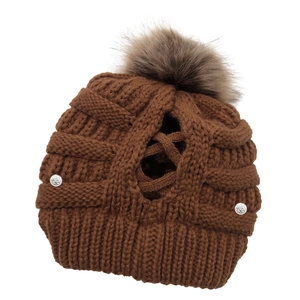 Detail of dark brown knit beanie showing the crisscross ponytail opening and fur pompom