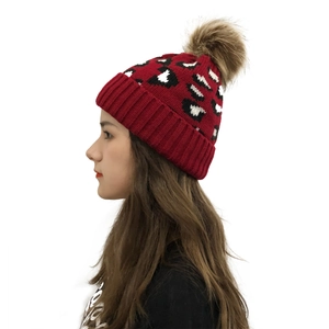 Detail of red leopard print knit beanie with faux fur pom pom on a female model