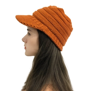 Close-up of orange chunky knit ski hat with visor brim worn by model on white background