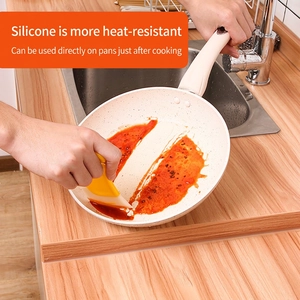Grattoir en silicone jaune résistant à la chaleur nettoyant la sauce d'une poêle blanche