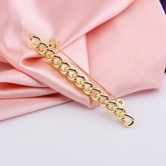 Golden curb chain brooch with long pin fastener on elegant pink satin fabric background