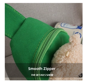 Close-up of green canvas chest bag with smooth zipper and cute plush bear pendant decoration