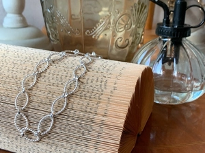 Macro detail of silver twisted rope oval link bracelet resting on vintage book pages