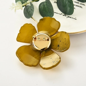 Elegante bernsteinfarbene Kamelien-Brosche aus Acryl mit goldener Nadel auf weißem Teller