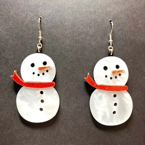 Detail of pearlescent white acrylic snowman earrings with glittery orange scarf accents