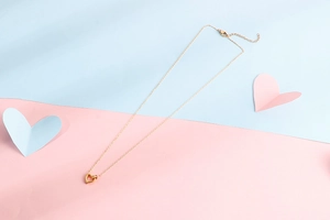 Detail of gold hollow heart pendant on a thin chain over a pink and blue background