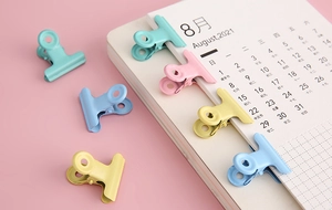 Close-up of colorful macaron metal binder clips on a pink desk calendar background
