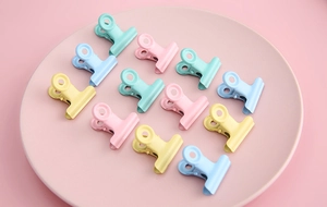 Colorful macaron metal clips in pink blue and yellow neatly arranged on a pink tray