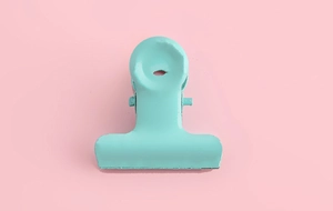 Detail of teal macaron metal binder clip on pink background for DIY crafting and school