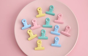 Close-up of colorful pastel metal binder clips on a pink ceramic plate for DIY projects