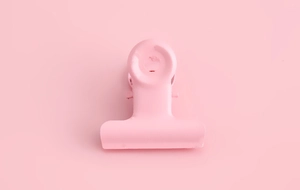 Detailed view of a pastel pink metal binder clip for DIY crafts and paper organizing