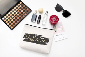 Detail view of linen cosmetic bag with You & Me text, surrounded by makeup items