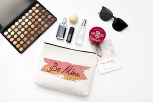 Flat lay of Be Mine canvas makeup bag with lipstick and perfume on white background