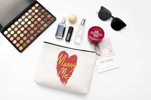 Flat lay of a white canvas makeup bag with a red heart and Marry Me text
