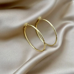 Minimalist gold hoop earrings featuring a polished finish on champagne silk background