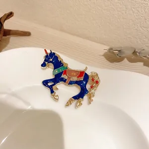 Cute enamel unicorn brooch in blue with gold trim on a white ceramic display plate