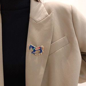 Detail of creative blue enamel horse brooch pinned on a stylish beige blazer lapel