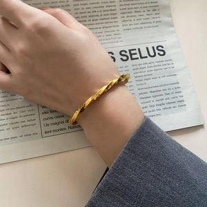 Detailansicht des goldenen Mobius Armreifs im gedrehten Design mit grauem Anzugärmel