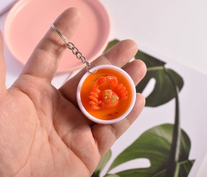 Realistic mini crab dish keychain with orange sauce in a white bowl, handheld for scale