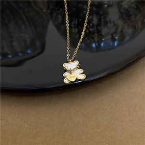 Macro detail of gold bear pendant with white enamel and heart charm engraved with Love