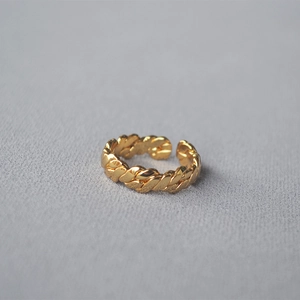 Detail eines handgefertigten vergoldeten geflochtenen Rings auf grauem Stoffhintergrund