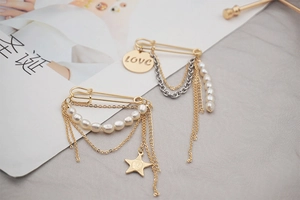 Detailed close-up of golden safety pin brooches with freshwater pearls and tassels