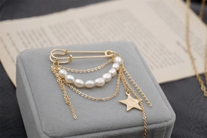 Detailed close-up of gold safety pin brooch with freshwater pearls and star charm