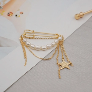 Golden safety pin brooch with freshwater pearls and tassel star pendant on grey fabric