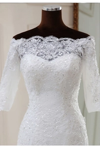 Détail de robe de mariée en dentelle à épaules dénudées avec sequins et manches longues