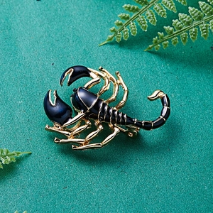 Fashionable scorpion brooch with black enamel inlay and gold-tone metal frame on green leaf