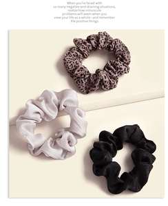 Close-up of leopard print, grey and black satin scrunchies set on a beige background